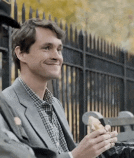 a man in a suit is eating a sandwich in front of a black fence