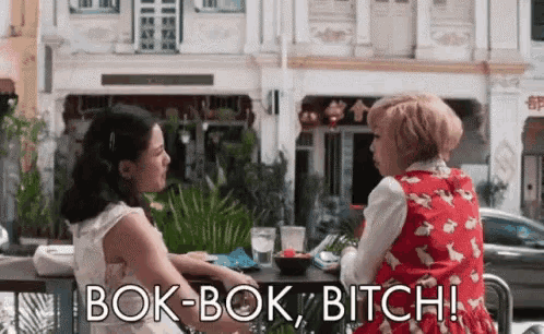 two women are sitting at a table in front of a building and one of them is talking to the other .
