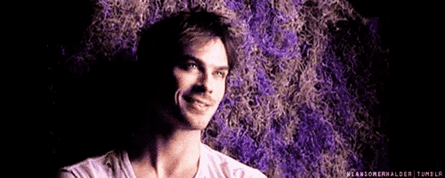 a man in a white shirt is smiling in front of a purple background