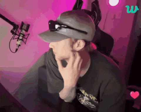 a man wearing a hat and sunglasses is sitting in front of a microphone in a room .
