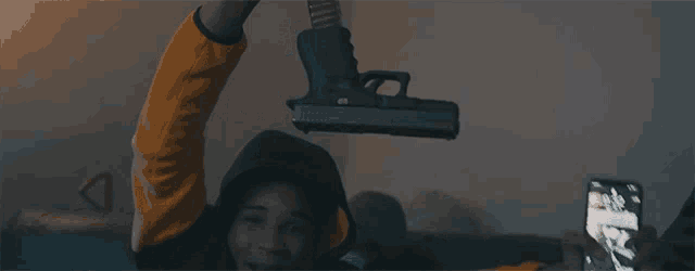 a person is holding a gun over their head and taking a picture with their phone