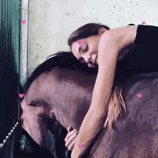 a woman is laying on top of a brown horse with pink hearts on it .