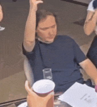 a man is sitting at a table with his arm in the air and a cup in his hand .