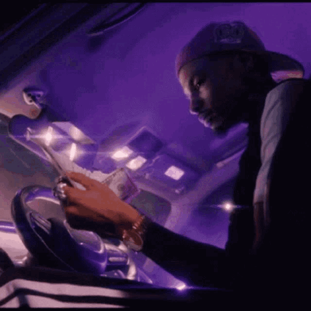 a man in a purple hat is sitting in the driver 's seat of a car counting money