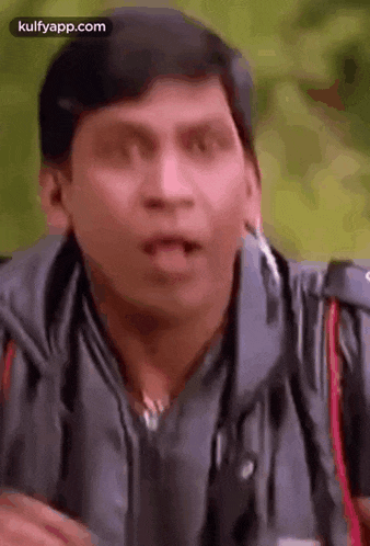 a man in a gray jacket is making a funny face with his mouth open .