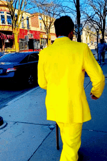a man in a bright yellow suit is walking down the street