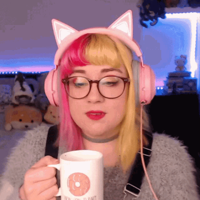 a woman wearing headphones and glasses holds a mug with a donut on it in front of her face