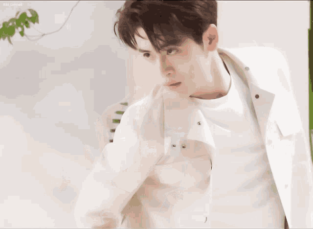 a man wearing a white jacket and a white shirt is standing in front of a white wall
