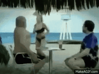 a group of people sitting at a table with a woman in a bikini dancing in the background .