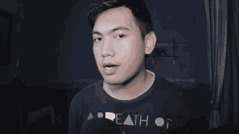 a man in a black shirt is making a funny face while talking in a dark room .