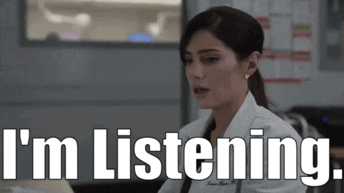 a woman in a lab coat says i 'm listening while sitting at a desk
