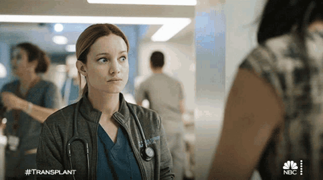 a woman with a stethoscope around her neck talks to another woman in a hospital hallway with the hashtag #transplant