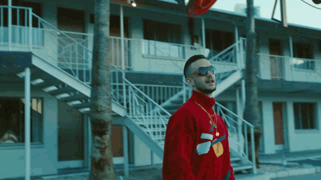 a man wearing sunglasses and a red sweater stands in front of a building with stairs