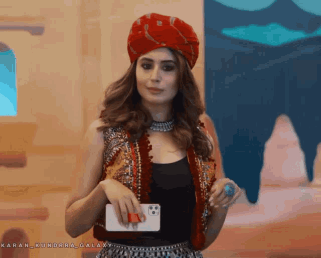 a woman wearing a red turban holds a cell phone in her hand