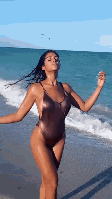 a woman in a metallic swimsuit is standing on the beach with her arms outstretched .