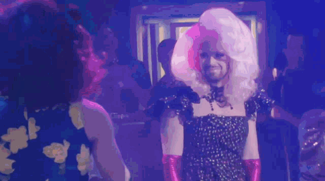 a woman in a floral dress stands next to a man in a drag queen costume