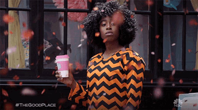 a woman in an orange and black striped shirt is holding a cup of coffee and confetti is falling around her