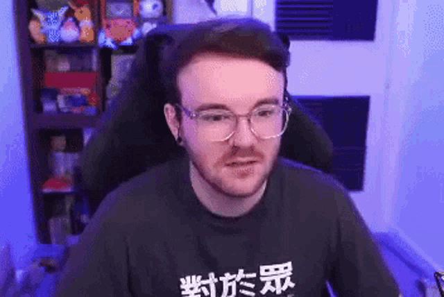 a man with glasses and a beard is sitting in a chair in front of a computer screen .