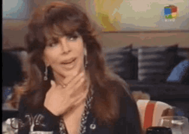 a woman with long hair is sitting at a table with her hand on her face .