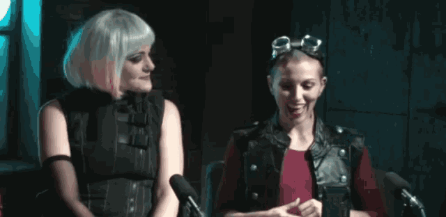 two women are sitting next to each other in front of microphones and smiling .