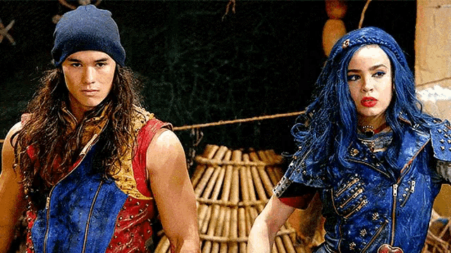 a man and a woman are standing next to each other . the woman has blue hair and the man has a beanie on .