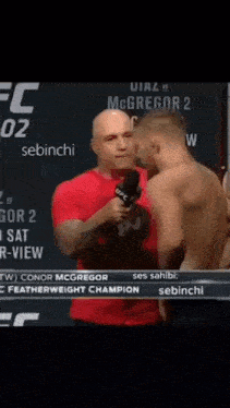 a man in a red shirt is holding a microphone and talking to another man in a red shirt
