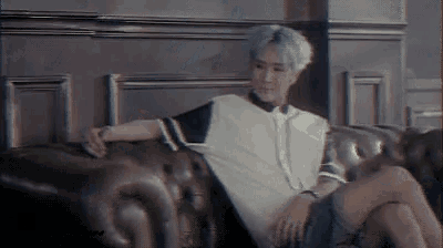 a man with blue hair is sitting on a leather couch with his legs crossed .