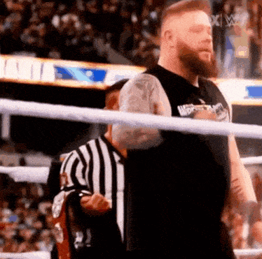 a wrestler is standing in a ring with a referee .