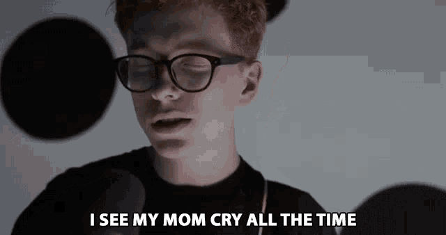 a young man wearing glasses says " i see my mom cry all the time " in front of a microphone
