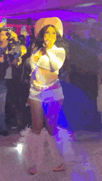 a woman in a cowboy hat is singing into a microphone at a party