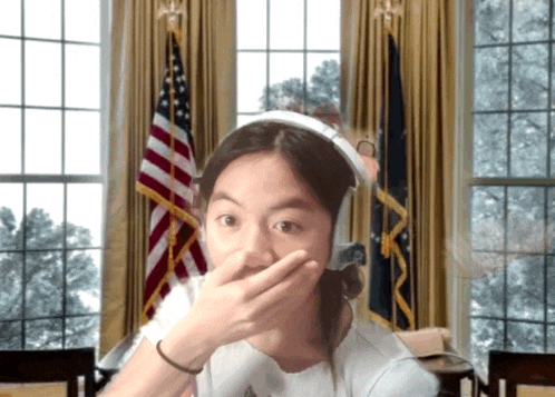 a woman wearing headphones covering her mouth with her hand in front of an american flag