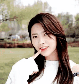 a woman with long hair and a white shirt is making a funny face with her finger in her mouth .
