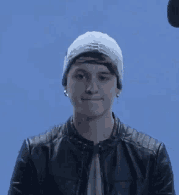 a young man wearing a beanie and a leather jacket is smiling .