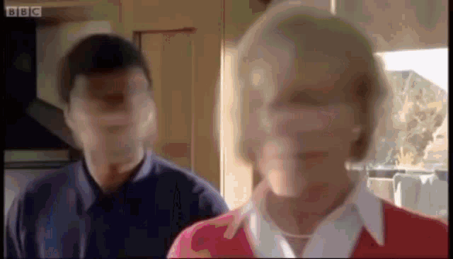 a man and a woman are standing next to each other in a kitchen . the woman is wearing a red sweater .