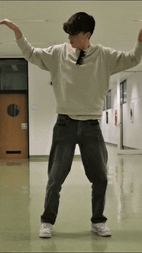 a young man in a white sweatshirt and black jeans stands in a hallway