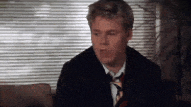 a man in a suit and tie is sitting on a couch and making a funny face .