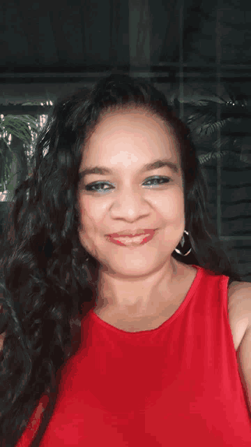 a woman wearing a red shirt and earrings smiles for the camera