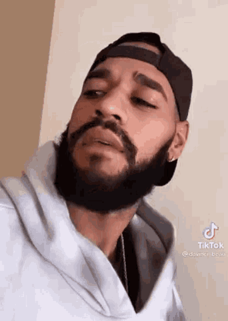 a man with a beard is wearing a baseball cap and a hoodie .