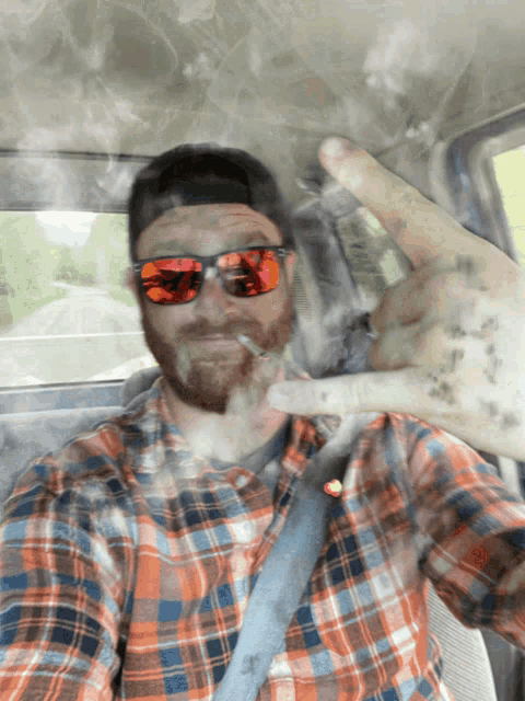 a man wearing sunglasses and a plaid shirt smoking a cigarette