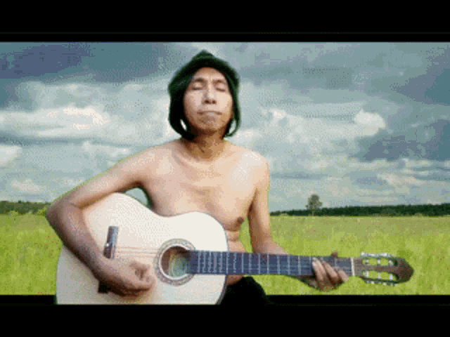 a shirtless man is playing a guitar in a grassy field