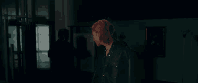 a man with pink hair is standing in a dark room with a man standing behind him .