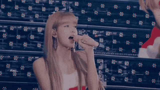 a woman singing into a pink microphone with a ring on her finger
