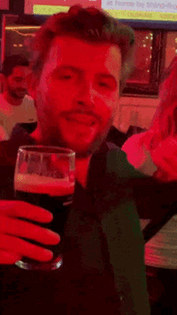 a man with a beard holds a glass of beer in front of him
