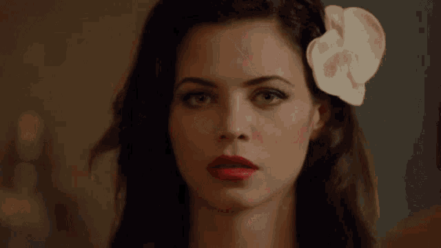 a woman with red lipstick and a white flower in her hair looks at the camera .