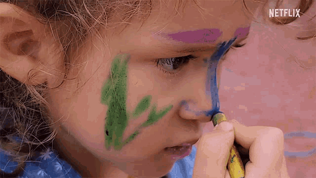 a little girl is painting her face with a crayon and the word netflix is visible in the corner .
