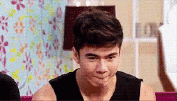 a young man in a black tank top is making a funny face in a room .