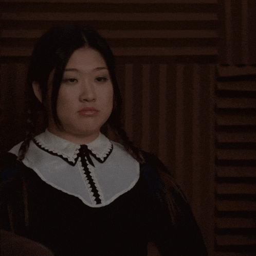 a woman in a black dress with a white collar is looking at the camera