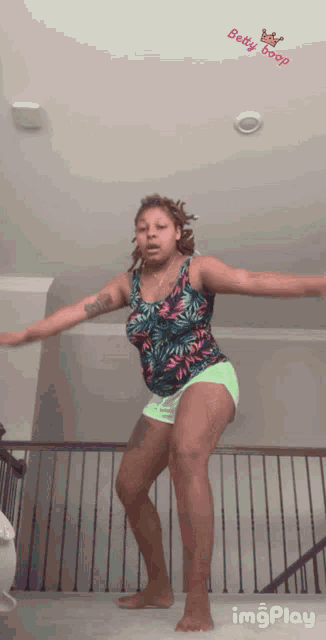 a woman in a tank top and shorts is dancing with a betty boop sticker on the ceiling above her