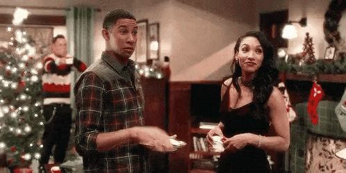 a man and a woman are standing next to each other in front of a christmas tree in a living room .