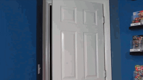 a white door is open in a room with a blue wall and a shelf with a video game on it .